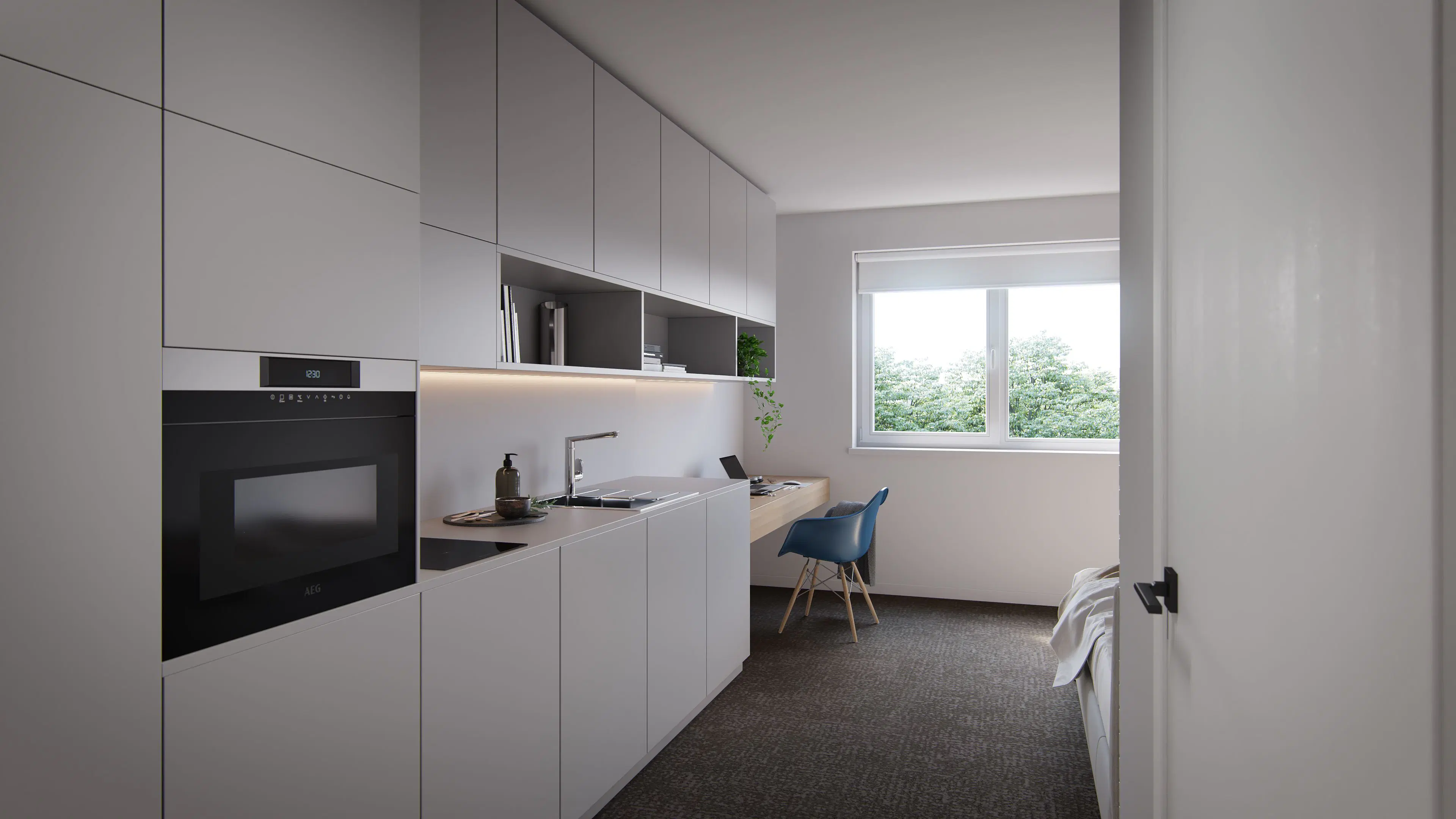 Espace compact et fonctionnel avec kitchenette intégrée et coin bureau. Une grande fenêtre apporte de la lumière naturelle et une vue sur la verdure.