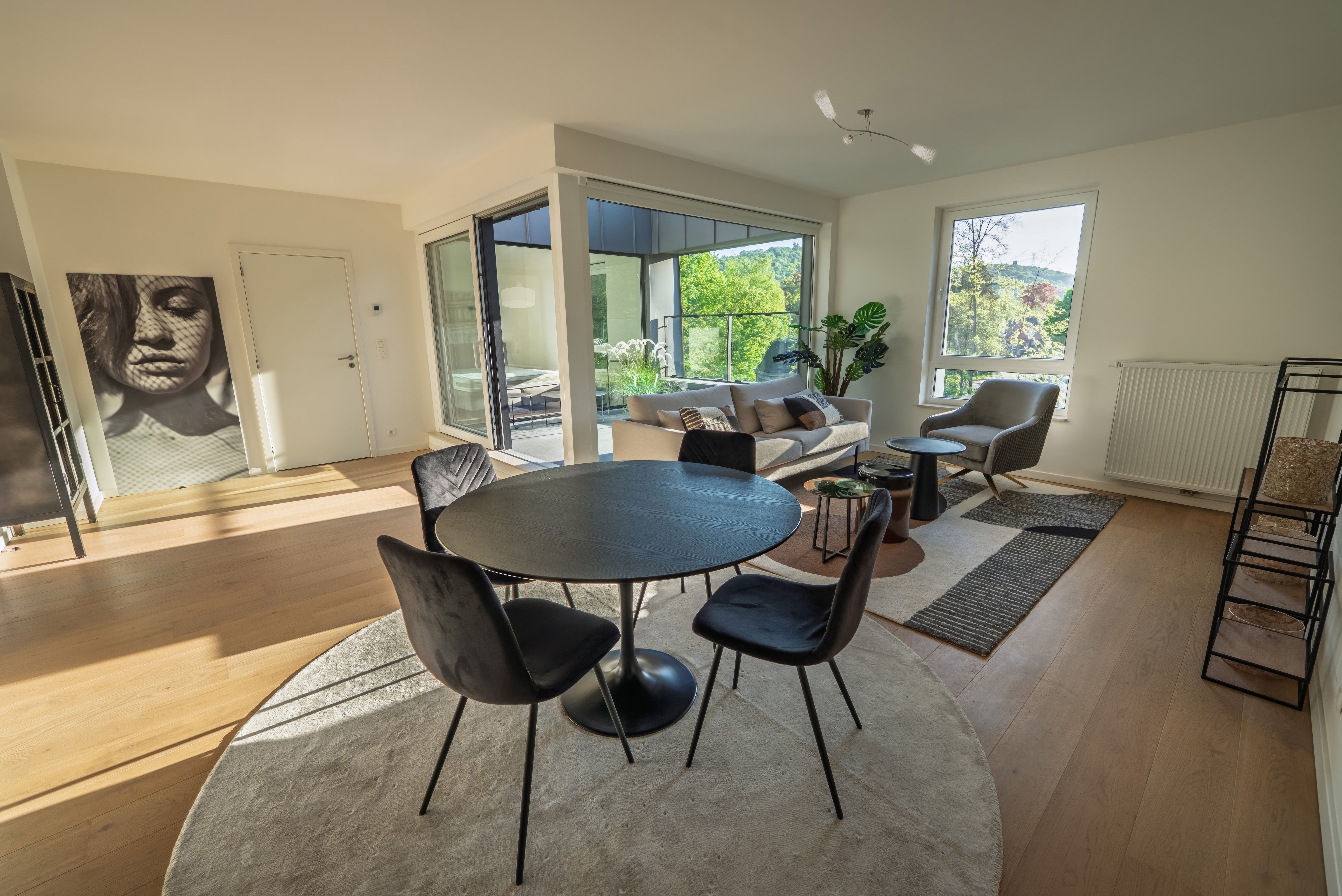 Séjour lumineux avec espace salon et salle à manger ouverts, aménagés dans un style contemporain. De grandes baies vitrées donnent accès à une terrasse et offrent une vue dégagée sur un environnement verdoyant.