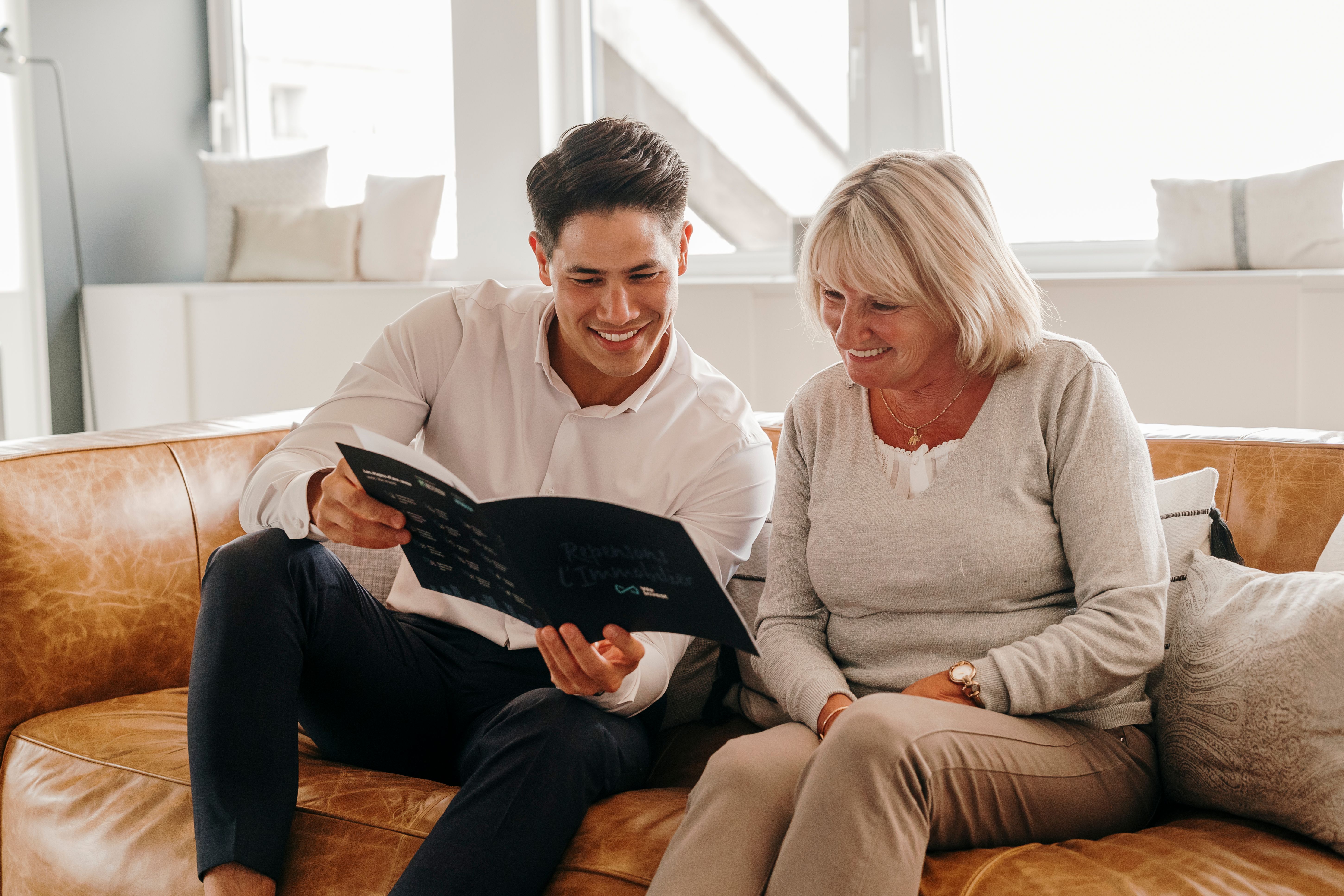 Owner sitting in a sofa with his We Invest real estate agent explaining the different steps of a sale.
