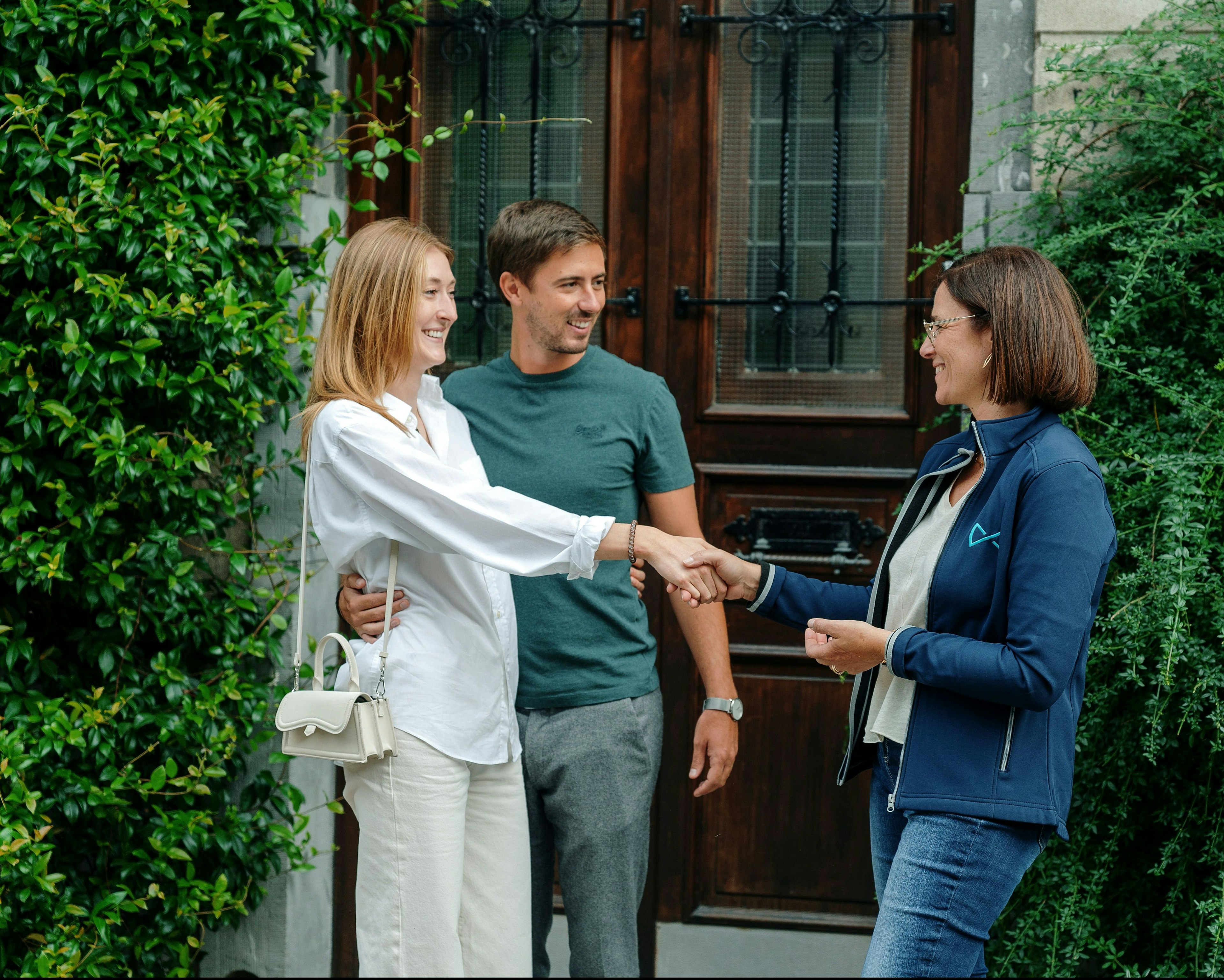 Un agent We Invest serre la main à un couple de propriétaires satisfaits devant leur maison pour conclure la vente.