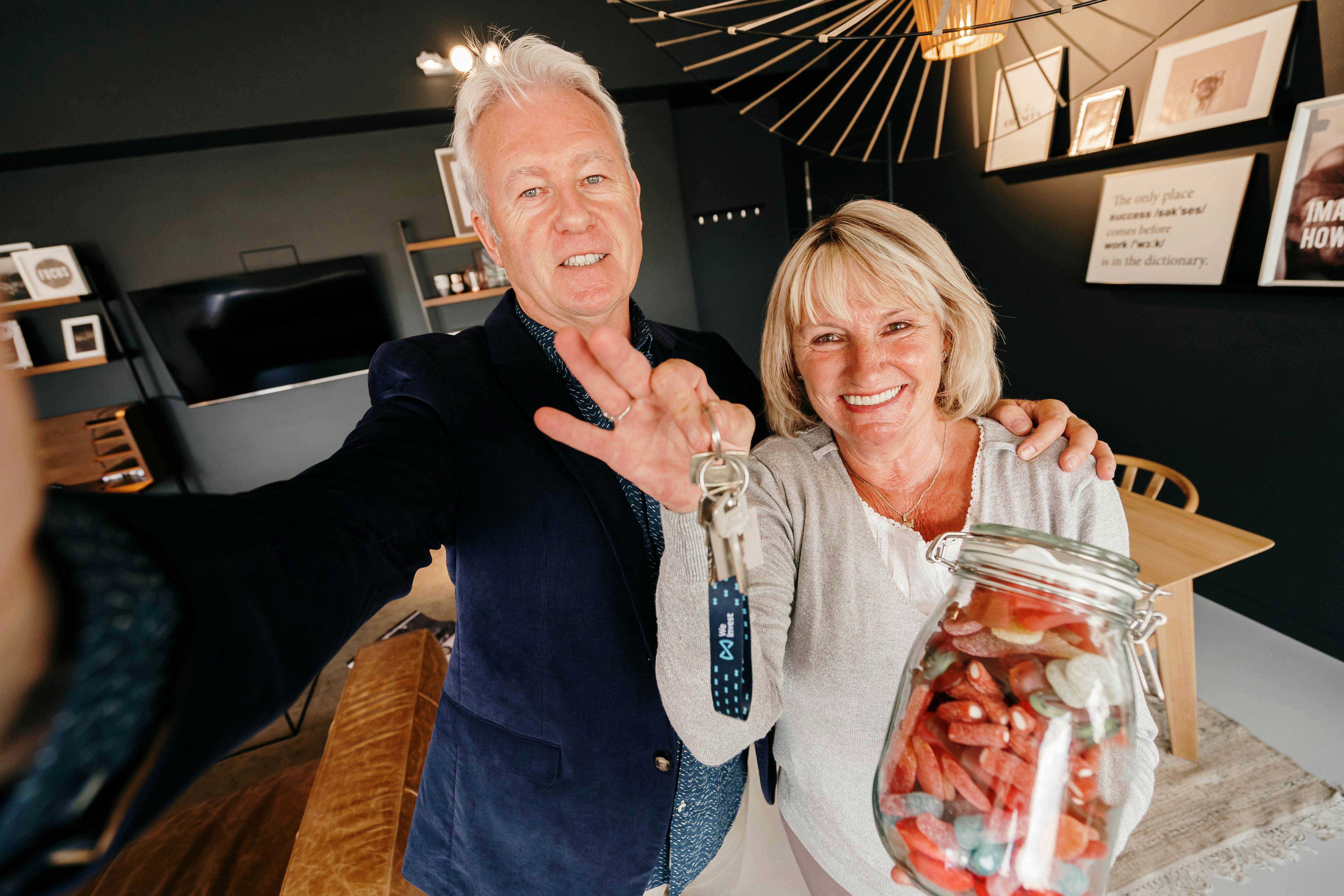 Couple senior heureux d'avoir vendu leur maison au meilleur prix grâce à leur agent We Invest tenant bonbonnière en main.