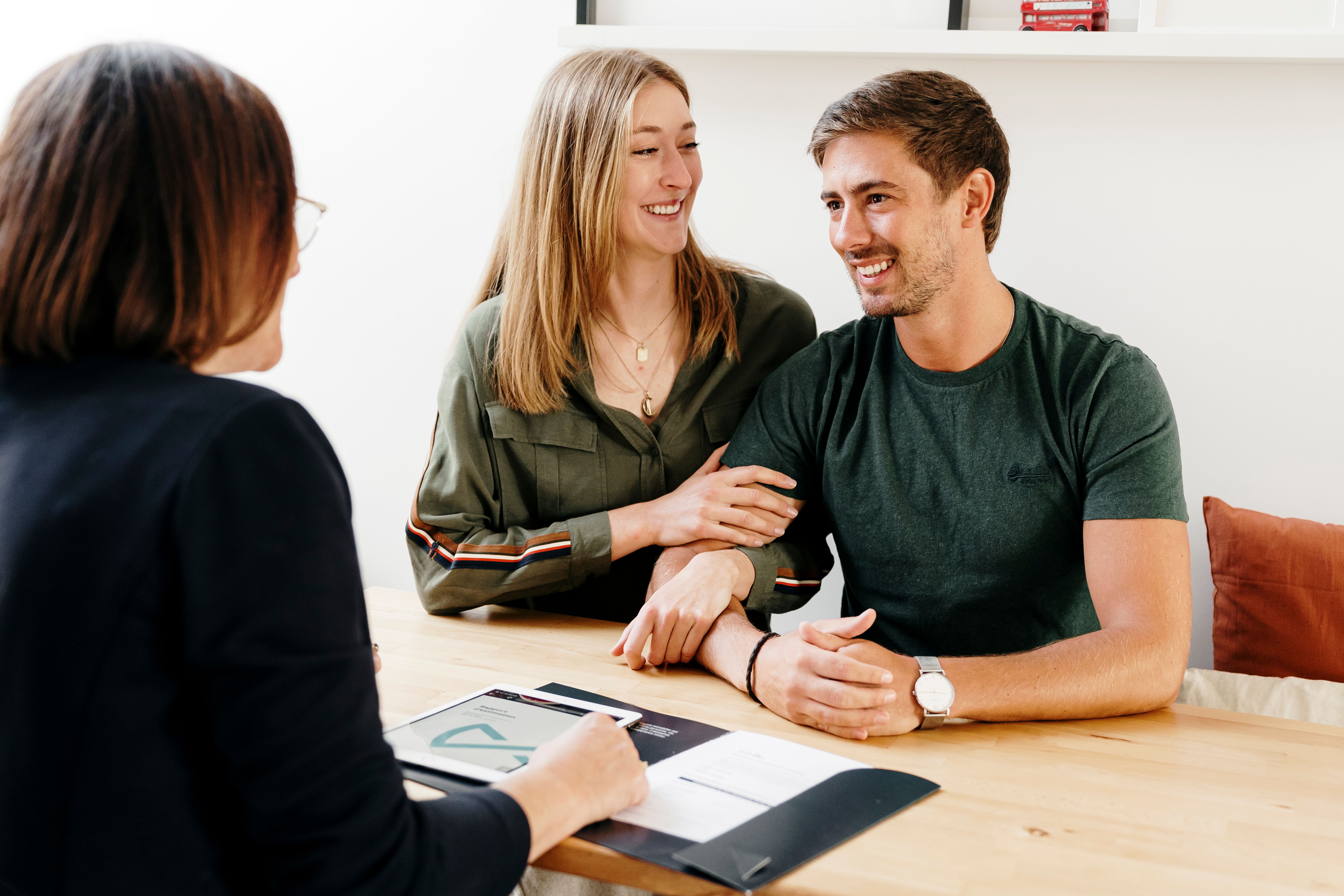 Agent immobilier et jeune couple d'acheteurs souriant autour d'une table pour acheter un appartement.